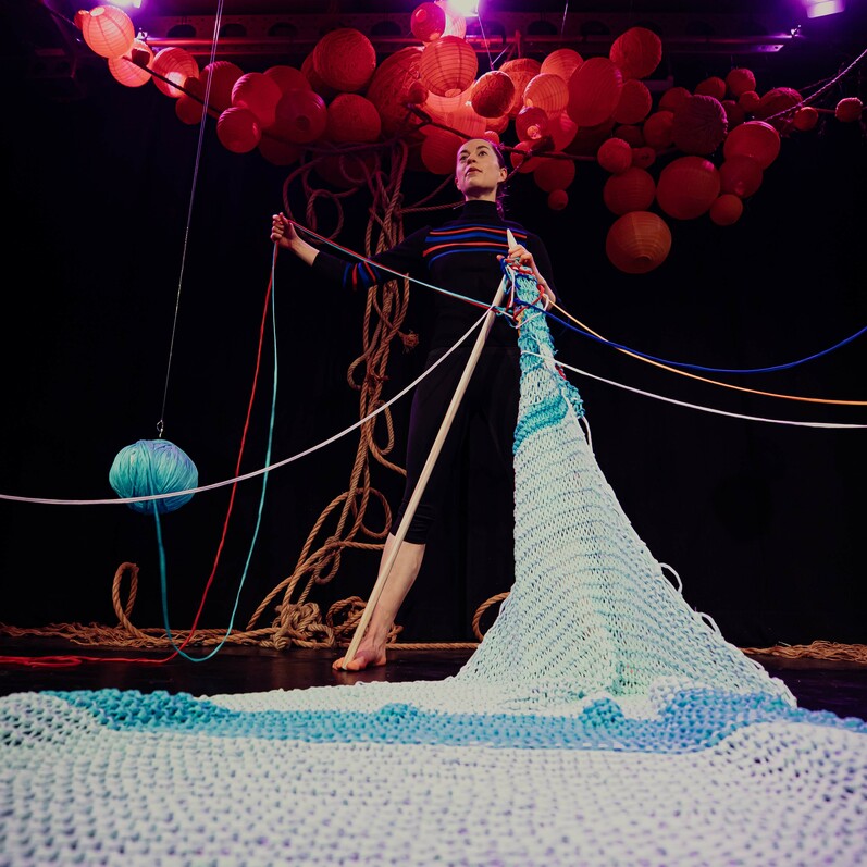 A performer with giant needles knitting
