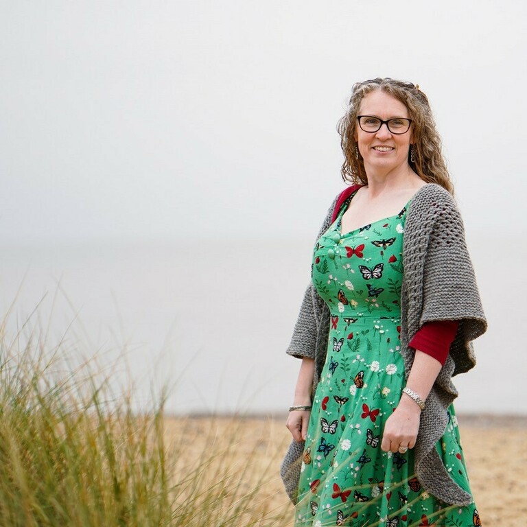 lady on a beach wearing a green dress and a grey shawl