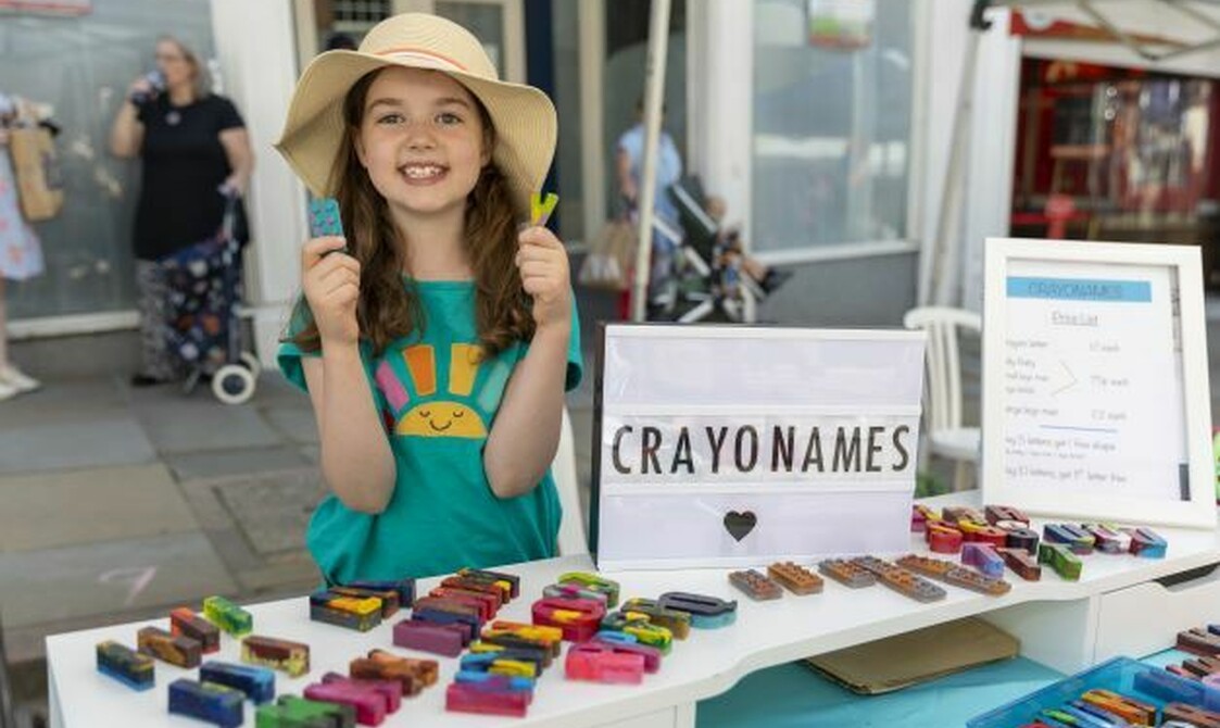 A girl holds up crayon blocks and smiles at the children's business Fair
