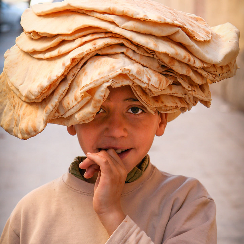 Young Syrian Boy with flatbreads piled on his head