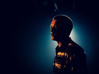 A man on a darkened background with a faint spotlight glowing behind him