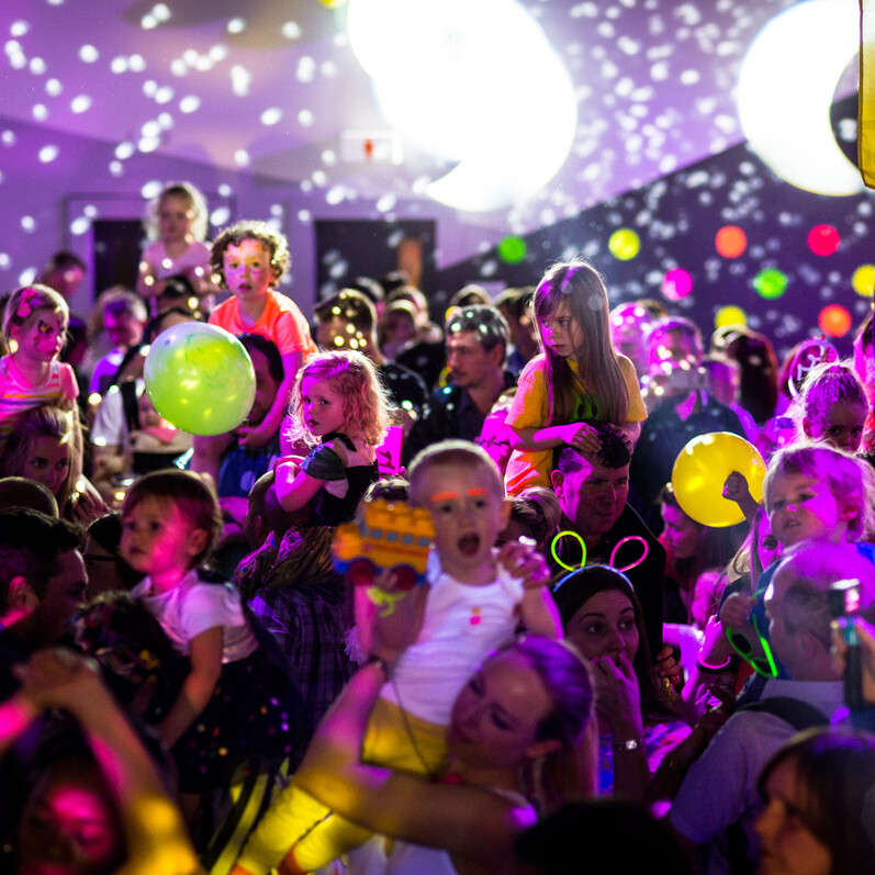 A colourful room full of children and adults with party balloons and confetti at the Big Fish little fish rave