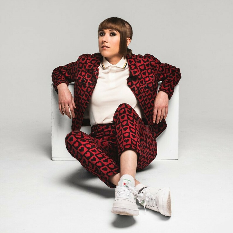Maisie Adam sitting on a floor wearing a suit with a red and black heart design