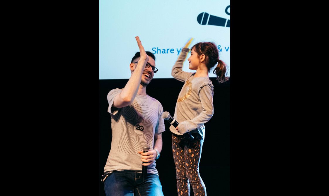 A young girl holding a microphone high fives a man kneeling beside her.
