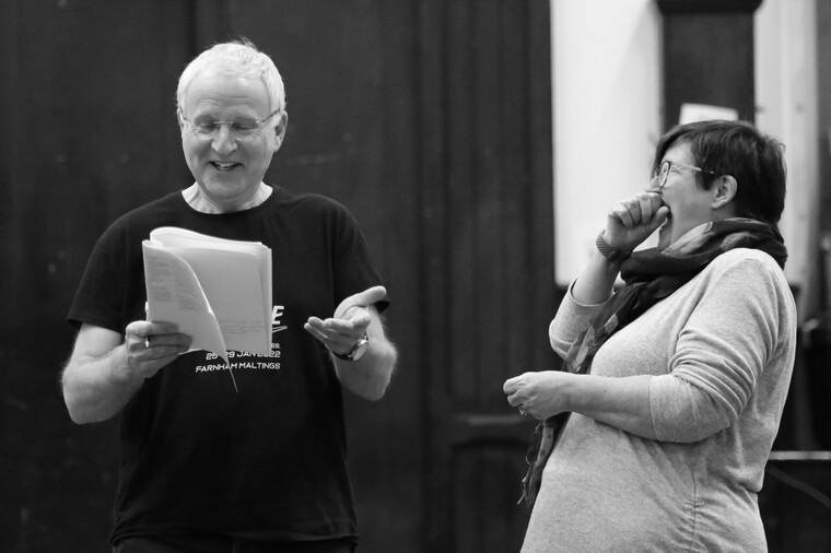 Grey-haired man holding script alongside woman laughing