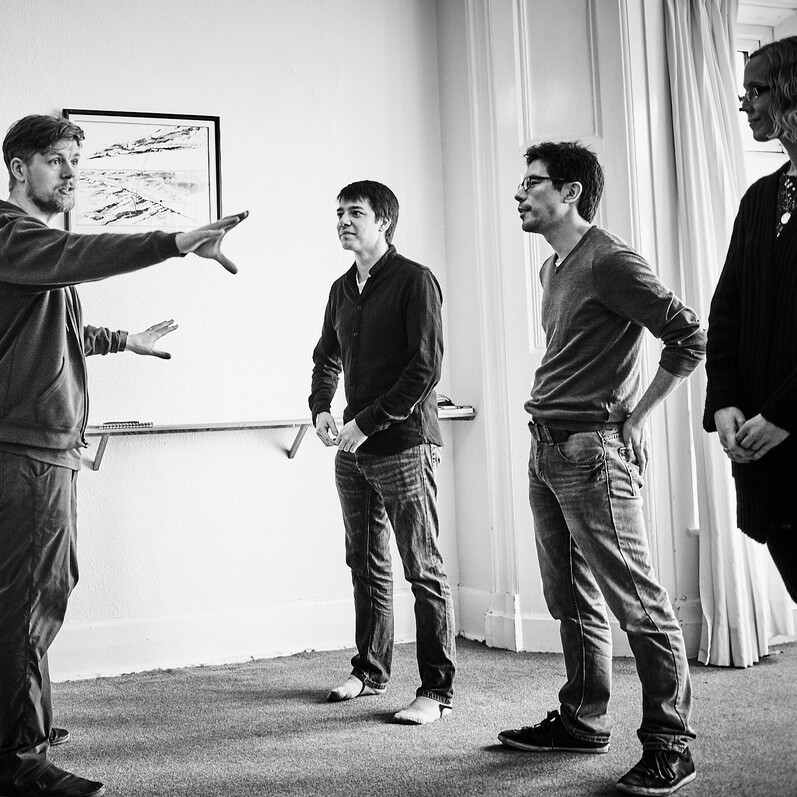 A black and white photo of a group of four adults standing in a room during an Improv comedy workshop.
