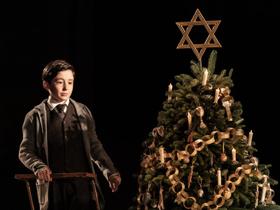 Young boy, Leo Roberts stands next to a decorated Christmas tree in a scene from NT Live's 'Leopoldstadt'