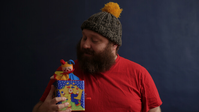 Jonny Donahoe wearing a bobble hat looks down at the jack in the box he is holding.