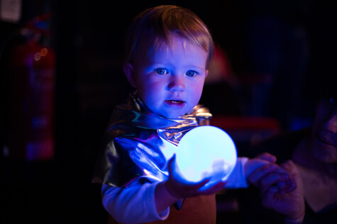 A baby holds a light orb at a showing of Kaleidoscope