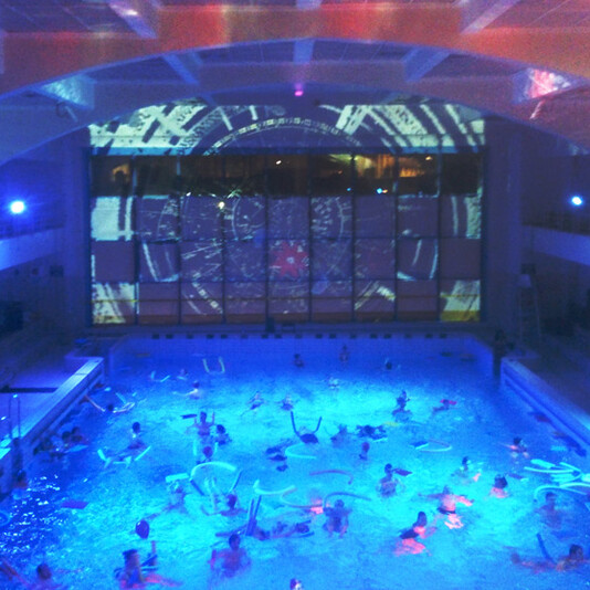 A light party in a large indoor swimming pool with swimming using floats.