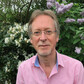 A head and shoulders image of a grey-haired man wearing glasses and a pink shirt