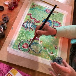 A hand holding a paint brush with ink over a batik print