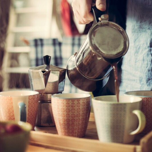 A hand pours coffee into mugs on a wooden tray